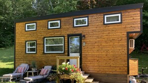 A wooden cabin with a porch, outdoor seating, and a small garden. - Charming Tiny House on 10 Wooded Acres (Richmond)