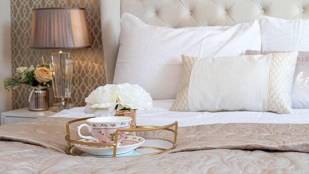 A neatly made bed with a tufted headboard, a bedside table with a lamp, and a decorative tray with a teacup and flowers. - Manchester - House - (Manchester)