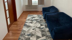 A room with a blue sofa, a patterned rug, wooden flooring, and a window with curtains. - 4-Bedroom House Sleeps 7 with Garden (Senec)