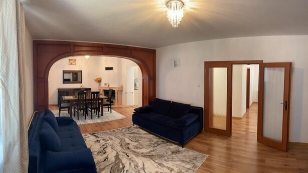 A living room with a dark blue sofa, a patterned rug, and a chandelier. - 4-Bedroom House Sleeps 7 with Garden (Senec)