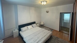 A bedroom with a bed, bedside table, chair, and a door leading to another room. - 4-Bedroom House Sleeps 7 with Garden (Senec)