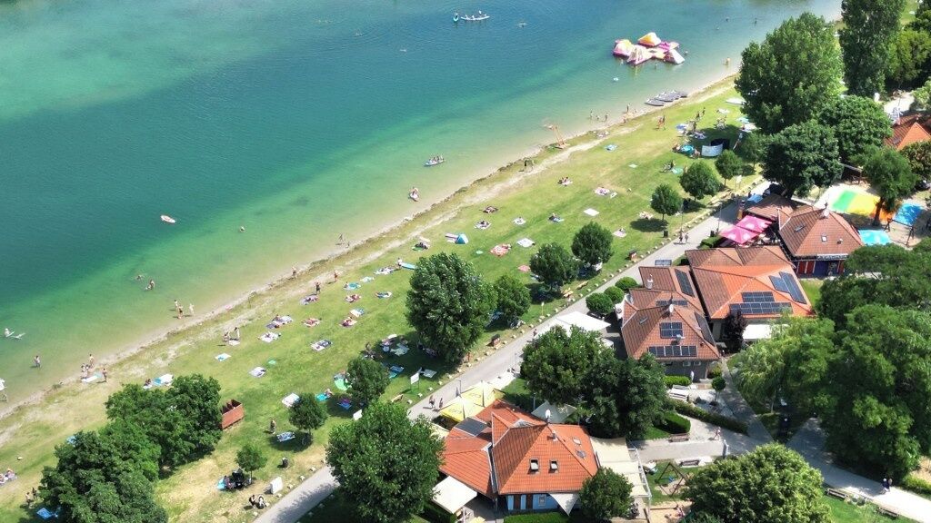 An aerial view of a coastal area with a beach, tents, and houses with red roofs.