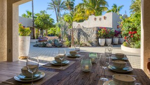 Un área de comedor al aire libre con vistas a un jardín y palmeras.