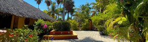Une maison à toit de chaume, entourée d’une végétation tropicale luxuriante, sous un ciel bleu azur.