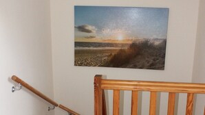 Eine Holztreppe mit Handlauf, mit Teppich ausgelegtem Boden und einem Strandbild an der Wand.