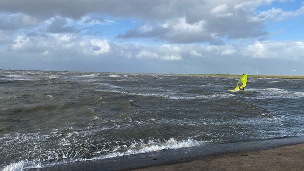 Ein Strand mit starken Wellen und eine Person beim Windsurfen.