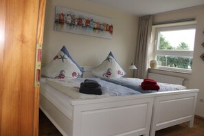 A double bed with two pillows, a bedside lamp, and a window with a view of greenery.