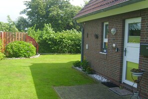 A brick house with a white door, a small garden with a lawn, and a wooden fence.