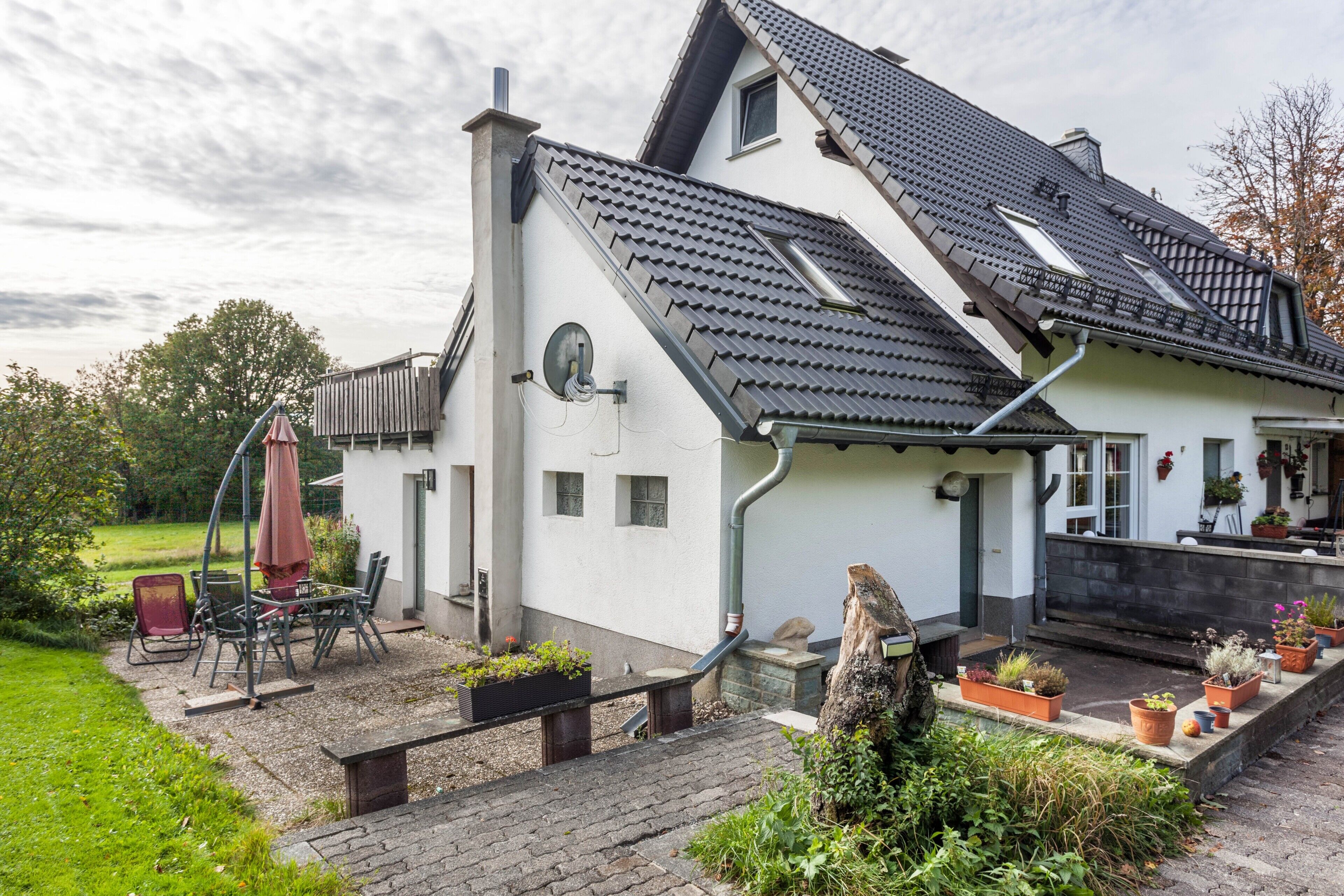 A house with a sloped roof, a garden with potted plants, outdoor furniture, and a chimney.