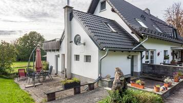 A house with a sloped roof, a garden with potted plants, outdoor furniture, and a chimney.