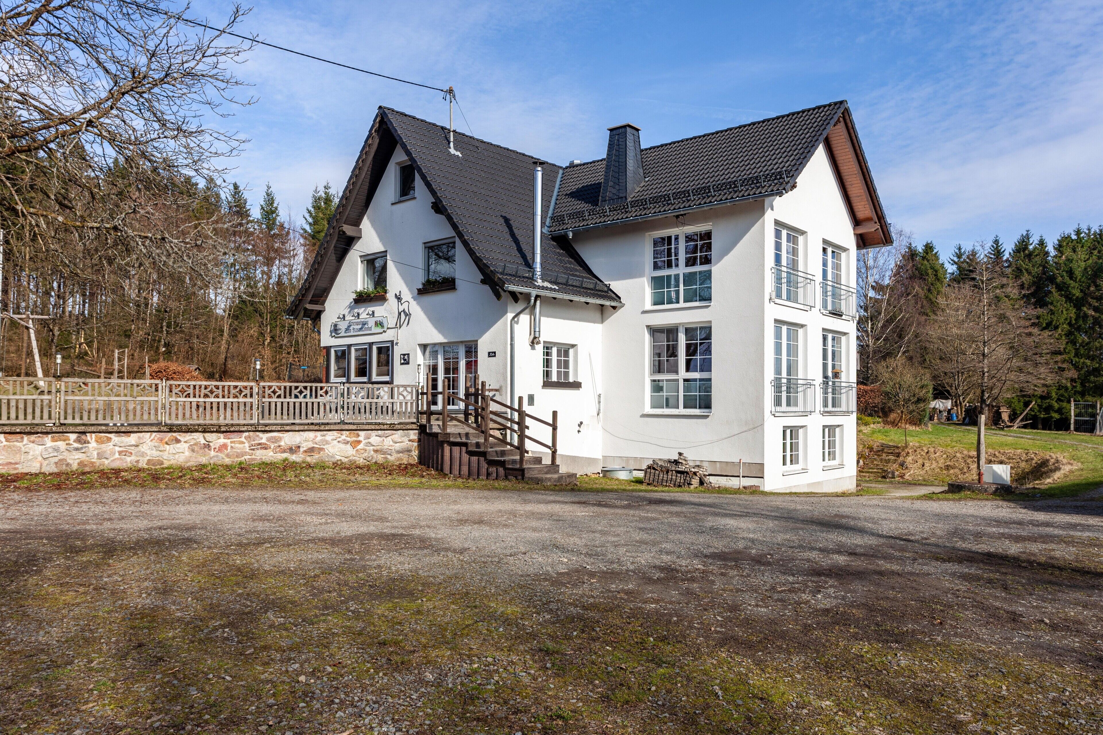 A two-story building with a stone wall, a wooden staircase, and a gravel driveway.