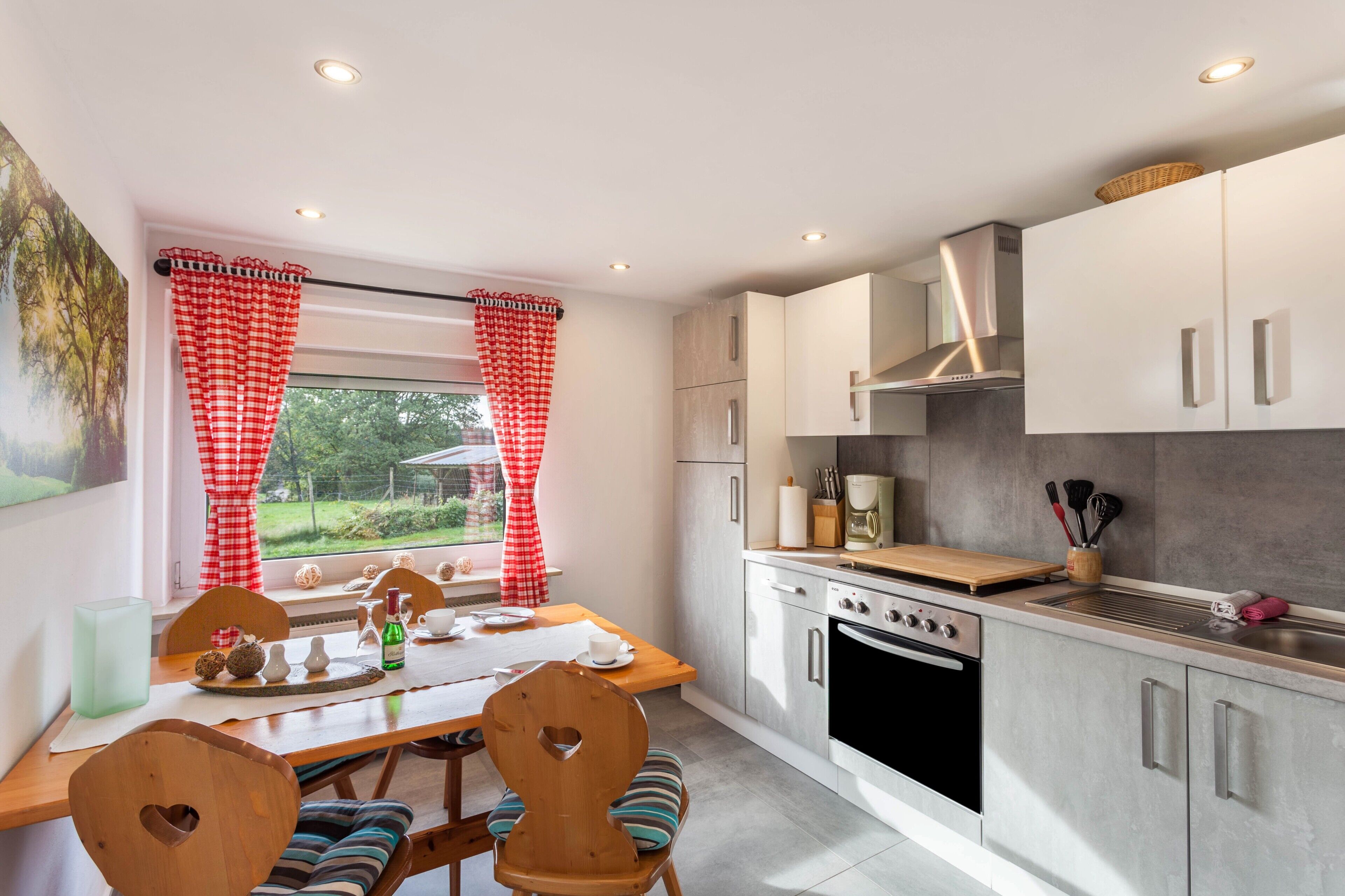 Una cocina moderna con armarios blancos, una campana de acero inoxidable y una zona de comedor con una mesa y sillas de madera.
