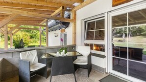 A covered outdoor seating area with wicker furniture and a glass table, a wooden ceiling, and a view of the garden. - Apartment No. 3 with terrace, 1 bedroom, max. 2 persons (Kirchhundem)
