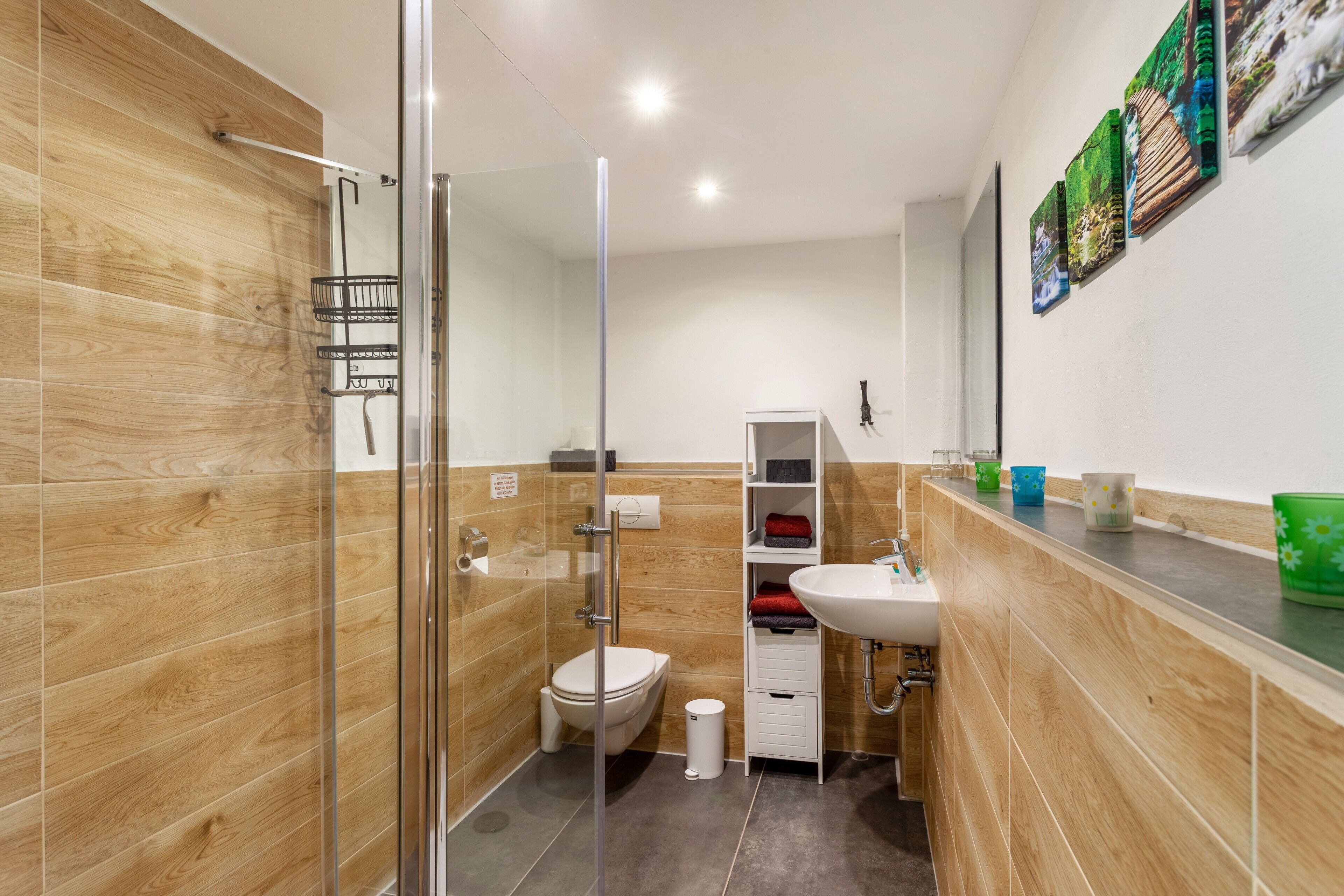 A modern bathroom with a glass shower enclosure, a white sink, and a wooden vanity.