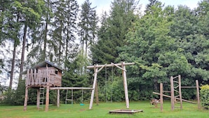 A wooden play structure with a swing and a slide, surrounded by a grassy area and dense trees. - Apartment No. 3 with terrace, 1 bedroom, max. 2 persons (Kirchhundem)