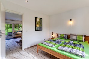 Ein Schlafzimmer mit einem Bett, einem Nachttisch, einer Wandleuchte und einer Tür, die auf einen Balkon führt.