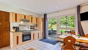 A modern kitchen with wooden cabinets, a built-in oven, and a dining area with a table and chairs. - Apartment No. 3 with terrace, 1 bedroom, max. 2 persons (Kirchhundem)