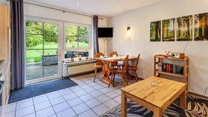 A modern room with a dining table, chairs, a bookshelf, a flat-screen TV, and a large window with curtains. - Apartment No. 3 with terrace, 1 bedroom, max. 2 persons (Kirchhundem)