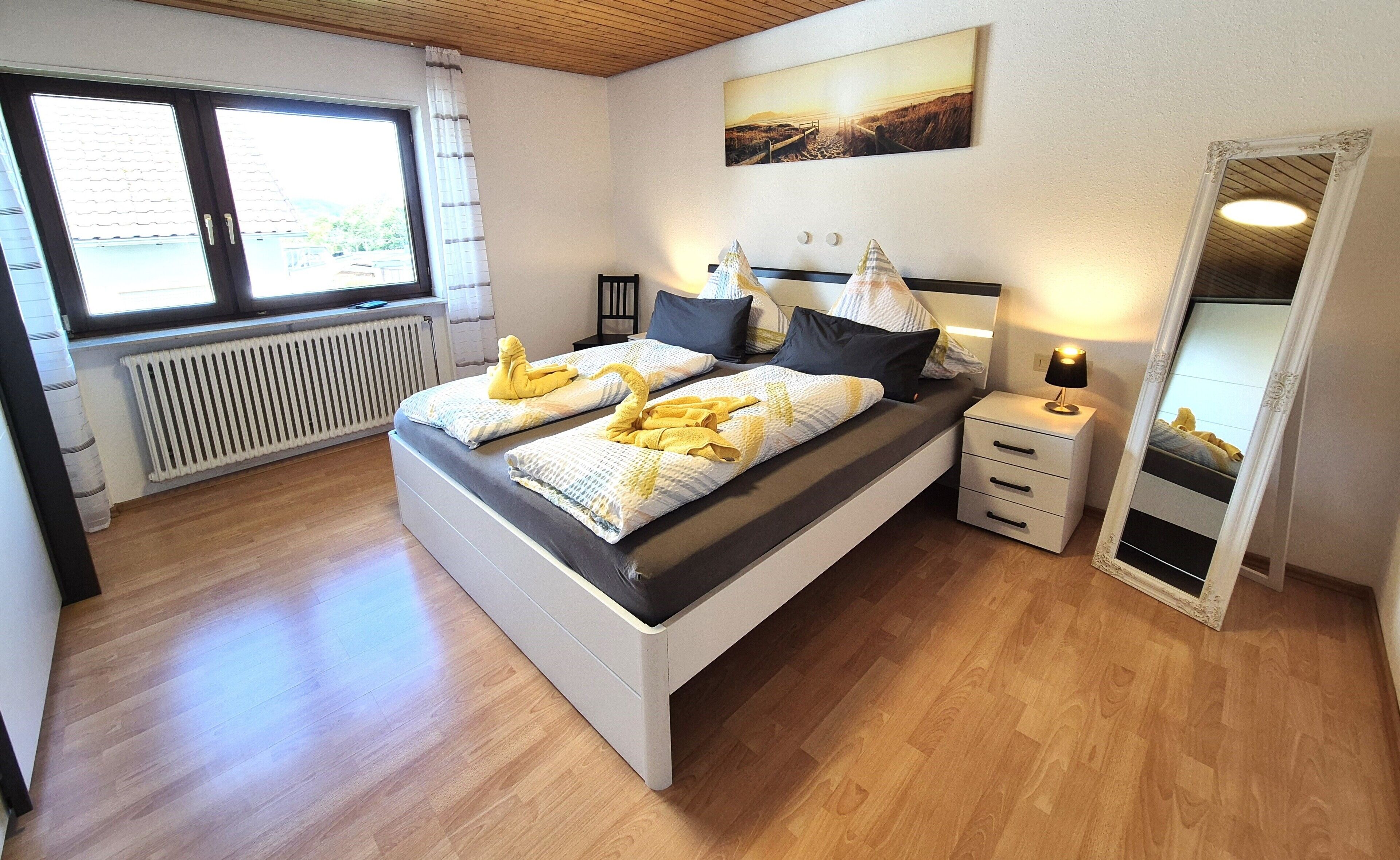 A bedroom with a bed, bedside tables, a mirror, a radiator, and a window.