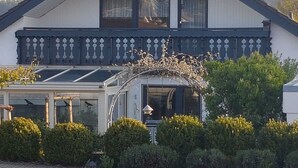 Una casa de dos pisos con balcón, invernadero y jardín.
