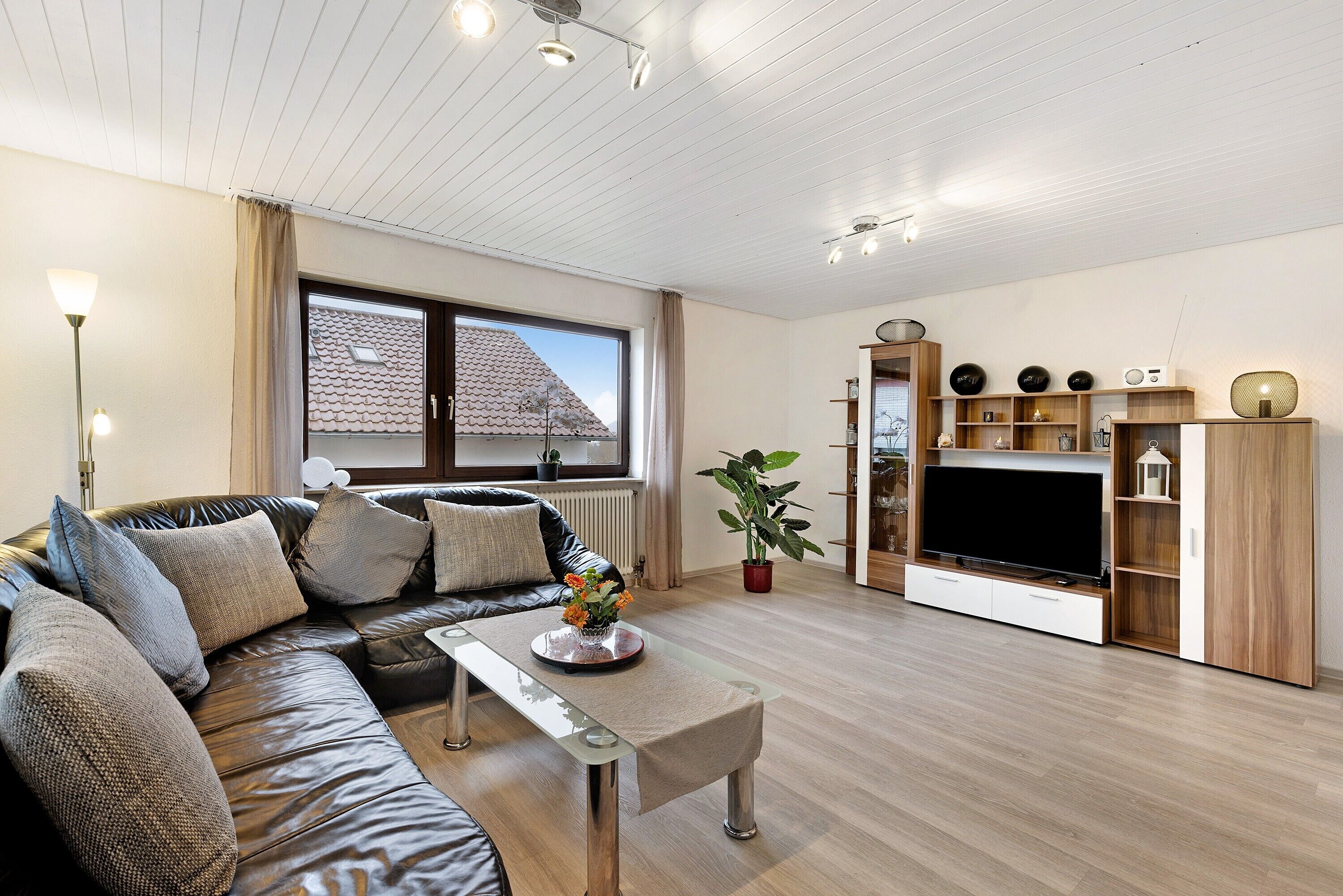 A modern living room with a leather sofa, a glass coffee table, a flat-screen TV, and a wooden entertainment unit.