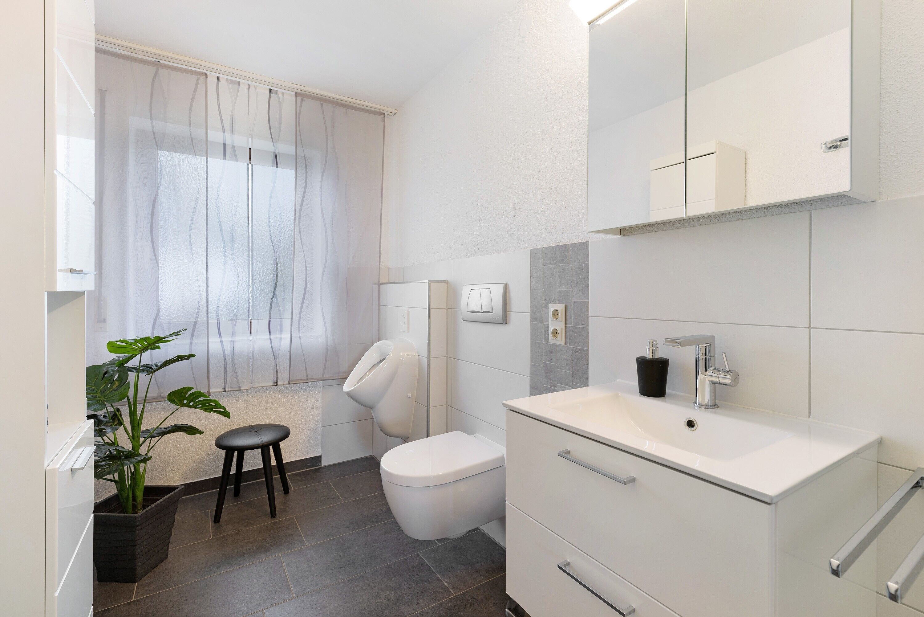 A modern bathroom with a toilet, bidet, sink, and a potted plant.