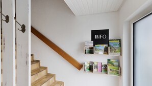 A staircase with a wooden handrail, a white wall with a sign reading 'INFO', and a window. - Vacation apartment Dahlie, 60 sqm, 1 bedroom, max. 3 persons (Münsingen)