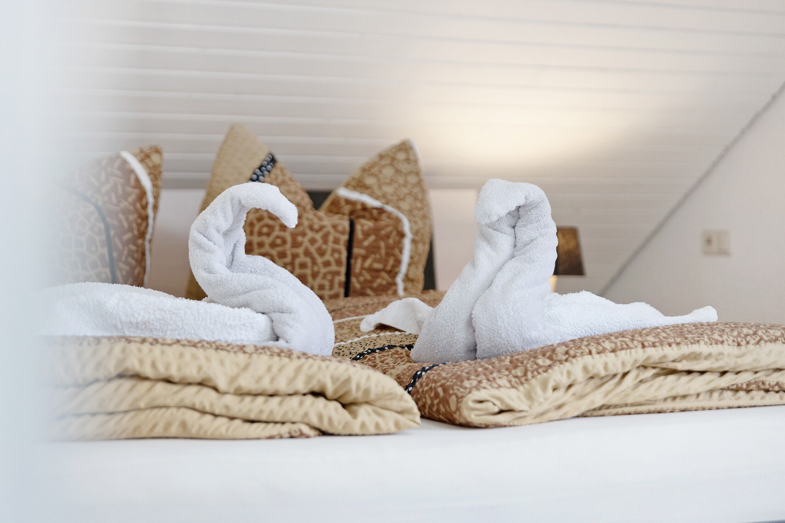 Un lit bien fait, avec des serviettes blanches, des coussins à motifs et une couverture à texture intéressante.