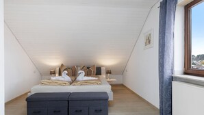 A bedroom with a sloped ceiling, a bed with decorative pillows, a bedside table with a lamp, and a window with curtains. - Vacation apartment Dahlie, 60 sqm, 1 bedroom, max. 3 persons (Münsingen)