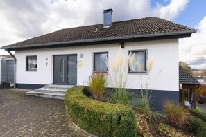 A white building with a tiled roof, numbered 16, and a small garden with plants and a hedge. - Vacation apartment Dahlie, 60 sqm, 1 bedroom, max. 3 persons (Münsingen)