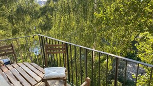 Een balkon met houten meubels, waaronder een bank en een tafel, met uitzicht op een dicht, groen bos.
