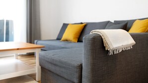 Een grijze bank met een witte deken, een geel kussen en een houten tafel in een moderne woonkamer.