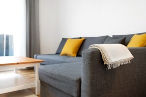 Un sofá gris con una manta blanca, un cojín amarillo y una mesa de madera en un moderno salón.
