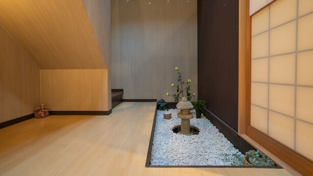 Un intérieur japonais traditionnel avec un sol recouvert de tatamis, un paravent shoji et un petit jardin agrémenté d’une lanterne en pierre et de plantes.