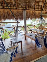 Una terraza de madera con dos columpios y un banco, con vista a un jardín y edificios.