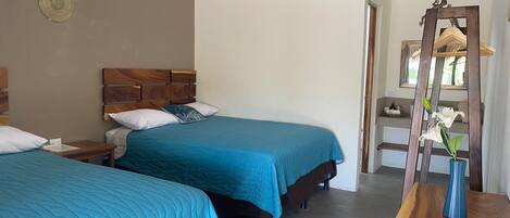Habitación de hotel con dos camas, cabecero de madera, mesita de noche, espejo y cómoda de madera.