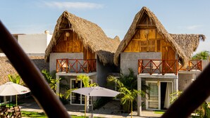 Two thatched-roof cottages with wooden balconies, a pool, and tropical plants.