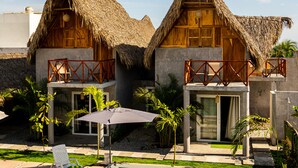 Two thatched-roof cottages with balconies, a pool, and tropical plants.