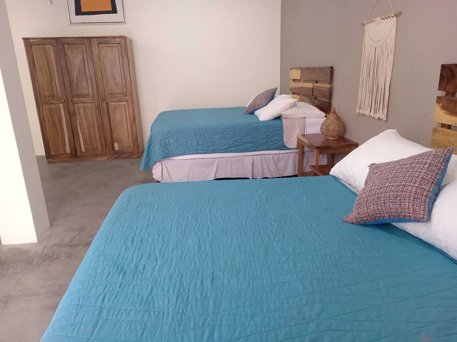A bedroom with two beds, a wooden wardrobe, and a macrame wall hanging.
