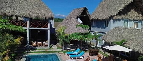 Un resort con cabañas de techo de paja, piscina y sillas de descanso.