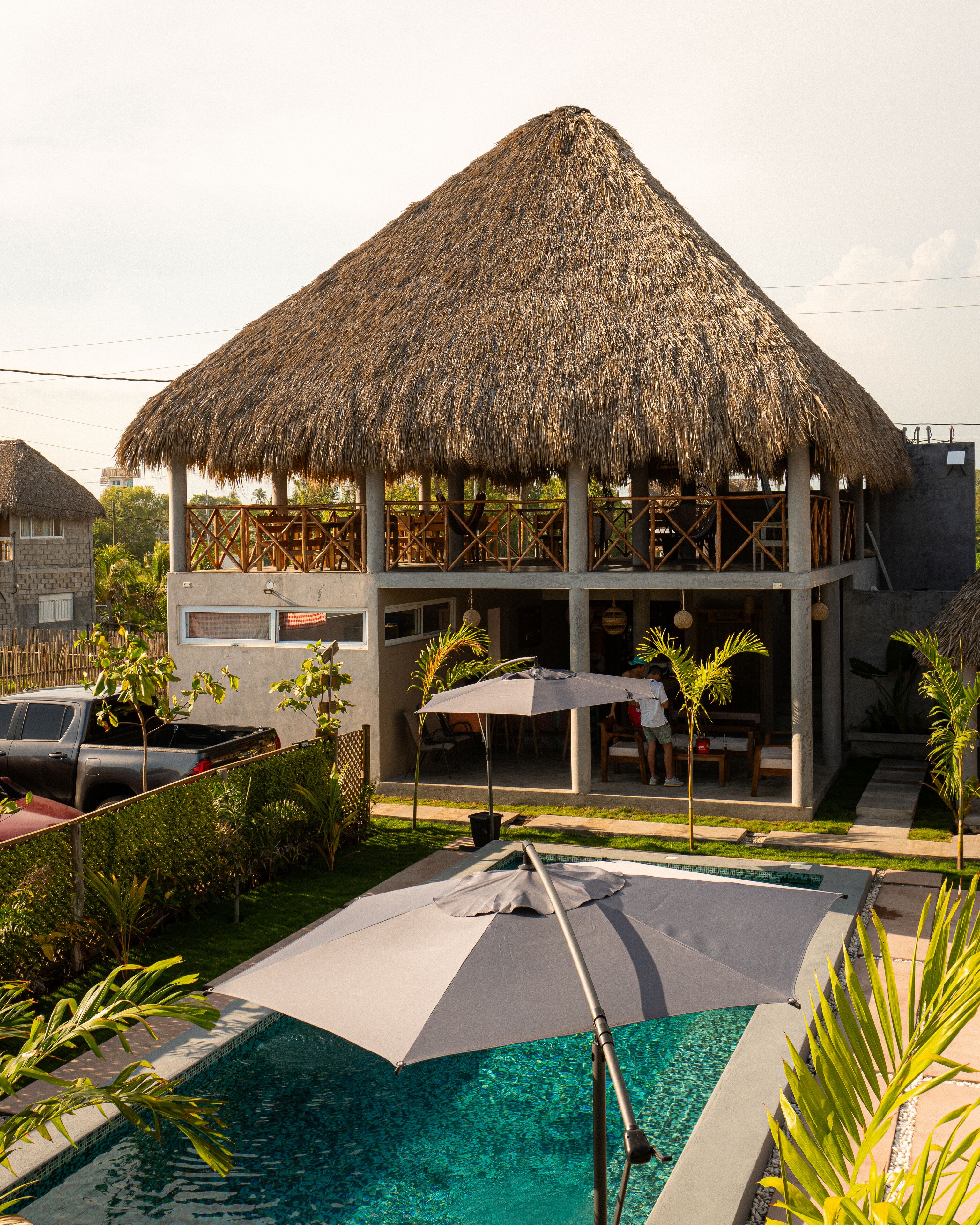 A resort with a thatched-roof structure, a swimming pool, and a car parked nearby.