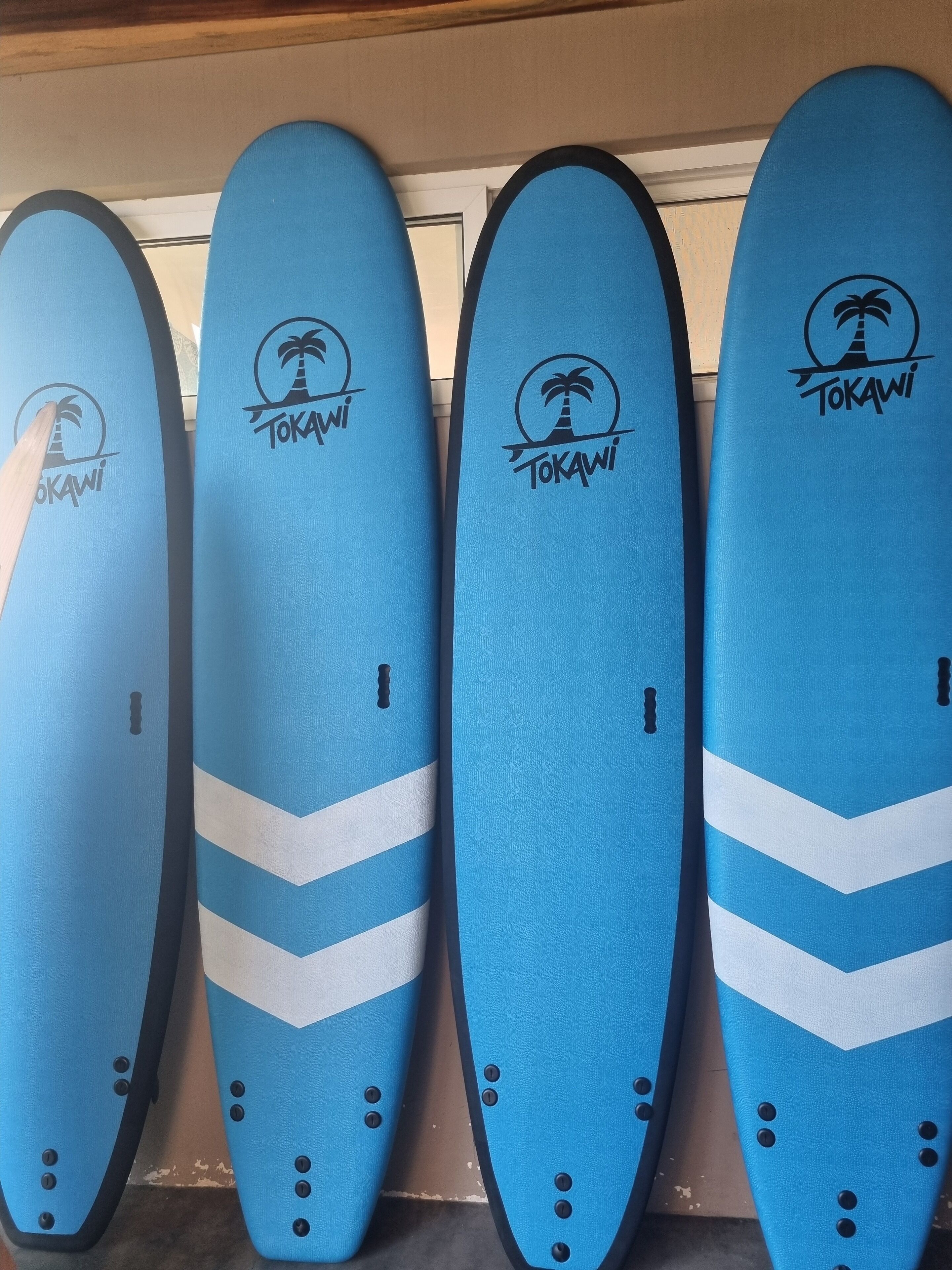 Four blue surfboards with the Tokawi logo and white chevron patterns, arranged side by side.