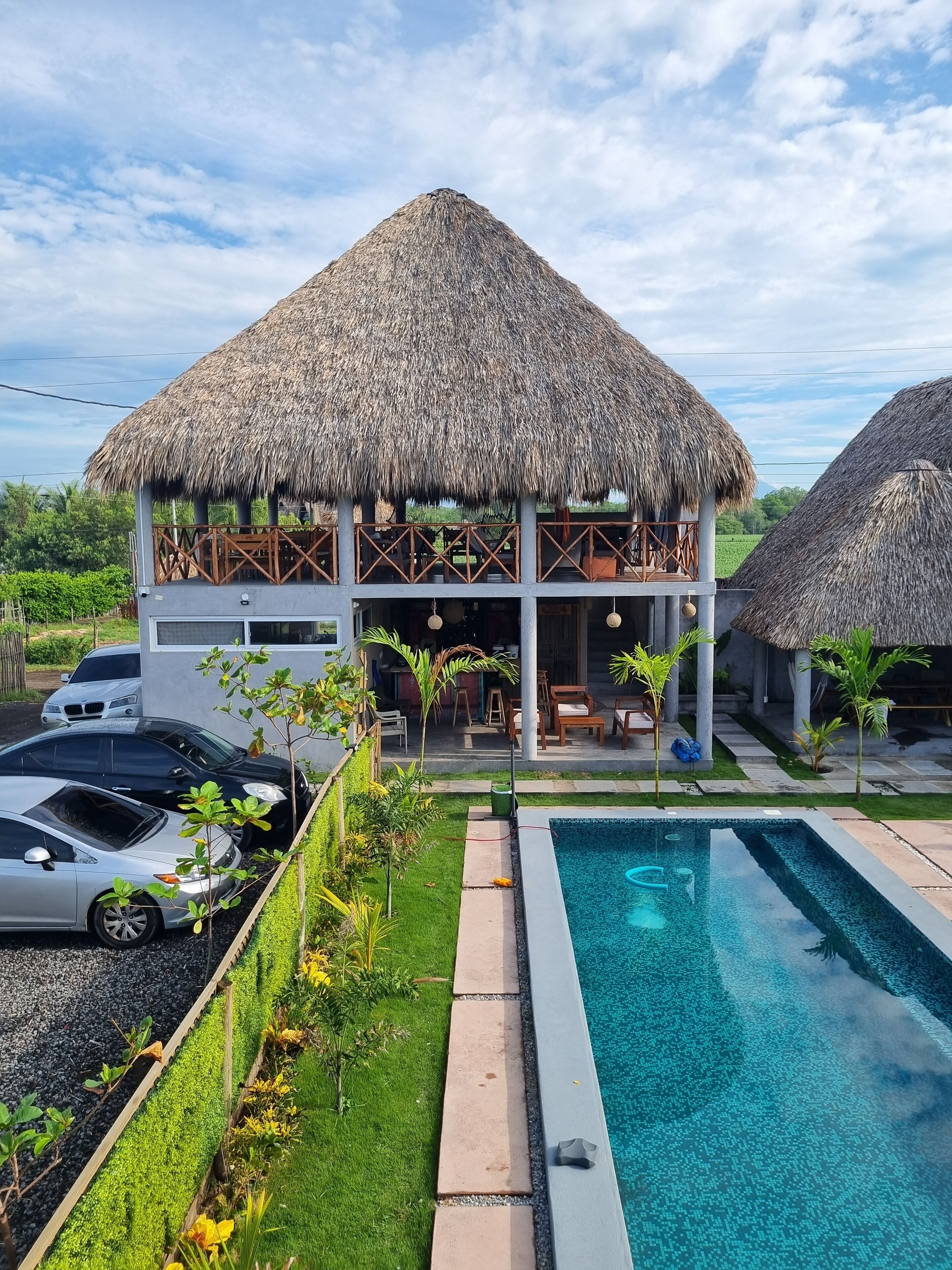Un complejo turístico con piscina, estructuras de techo de paja y un jardín.