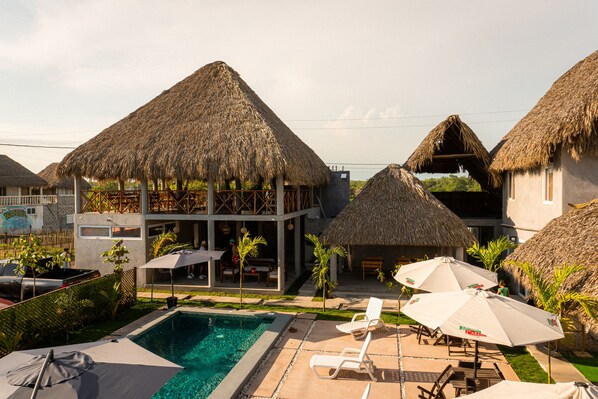 A resort with thatched-roof buildings, a swimming pool, and outdoor seating areas.