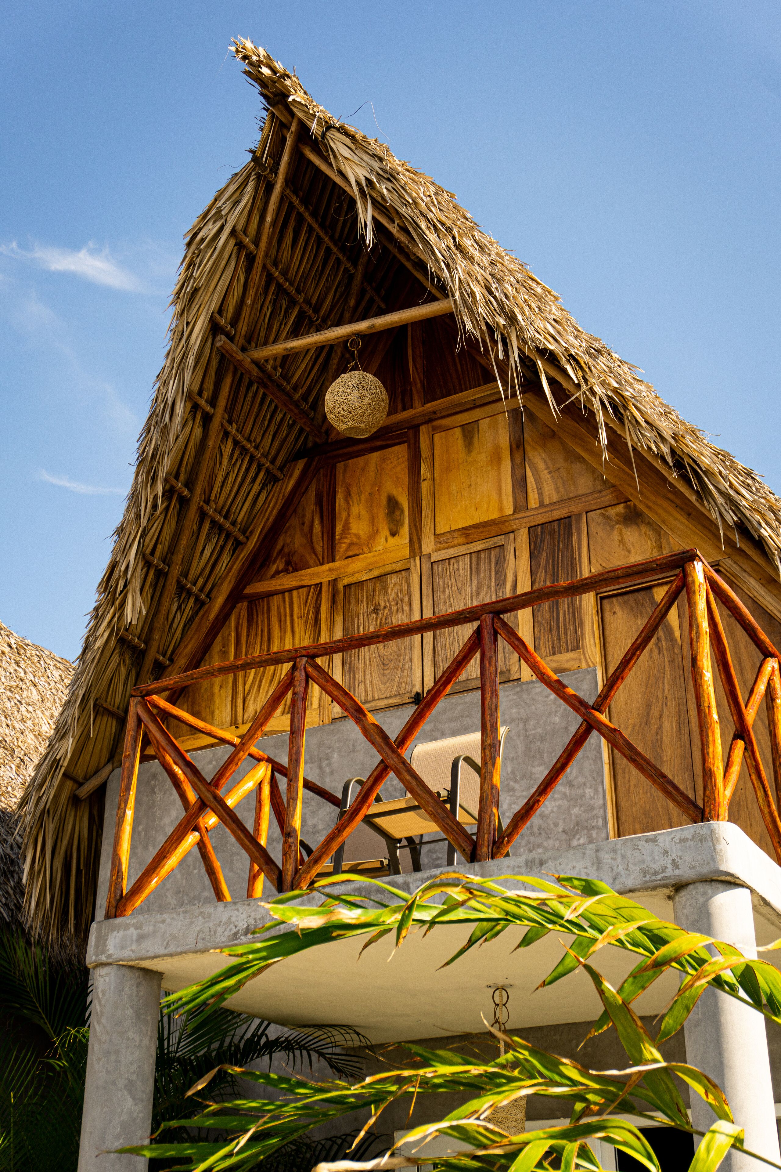 A thatched-roof building with a wooden balcony and a concrete base.