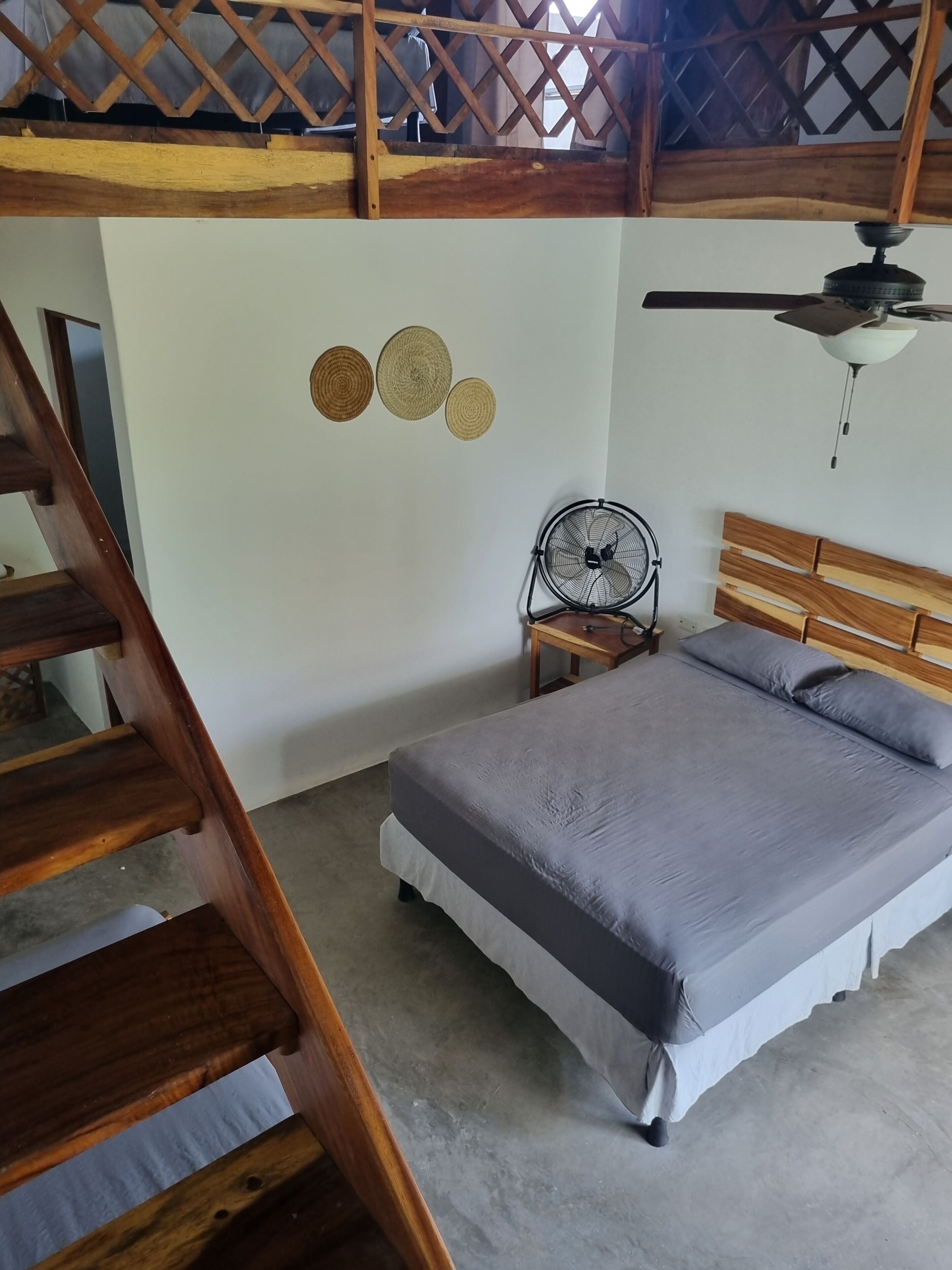 Une chambre à coucher avec un lit en bois, un ventilateur sur pied et un ventilateur de plafond.