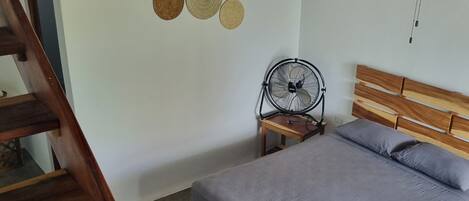Un dormitorio con cama de madera, un ventilador de pie y un ventilador de techo.