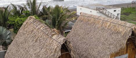A beachfront property with thatched-roof huts, a staircase leading to a deck, and a view of the ocean.