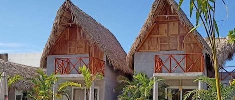 Un complexe hôtelier doté de bungalows aux toits de chaume, d’une piscine et de chaises longues.