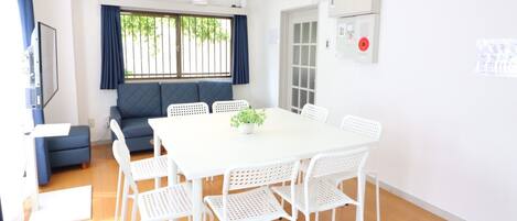 A modern room with a white table, six white chairs, a blue sofa, and a large window with blue curtains.